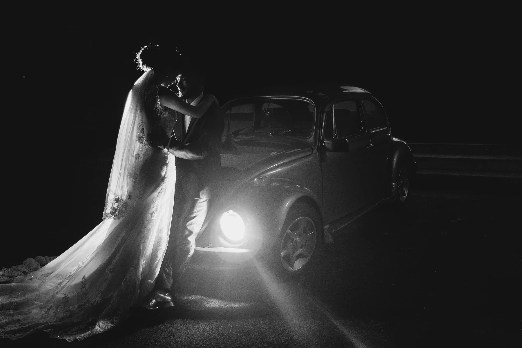 Noivos em retrato noturno ao lado de um carro clássico