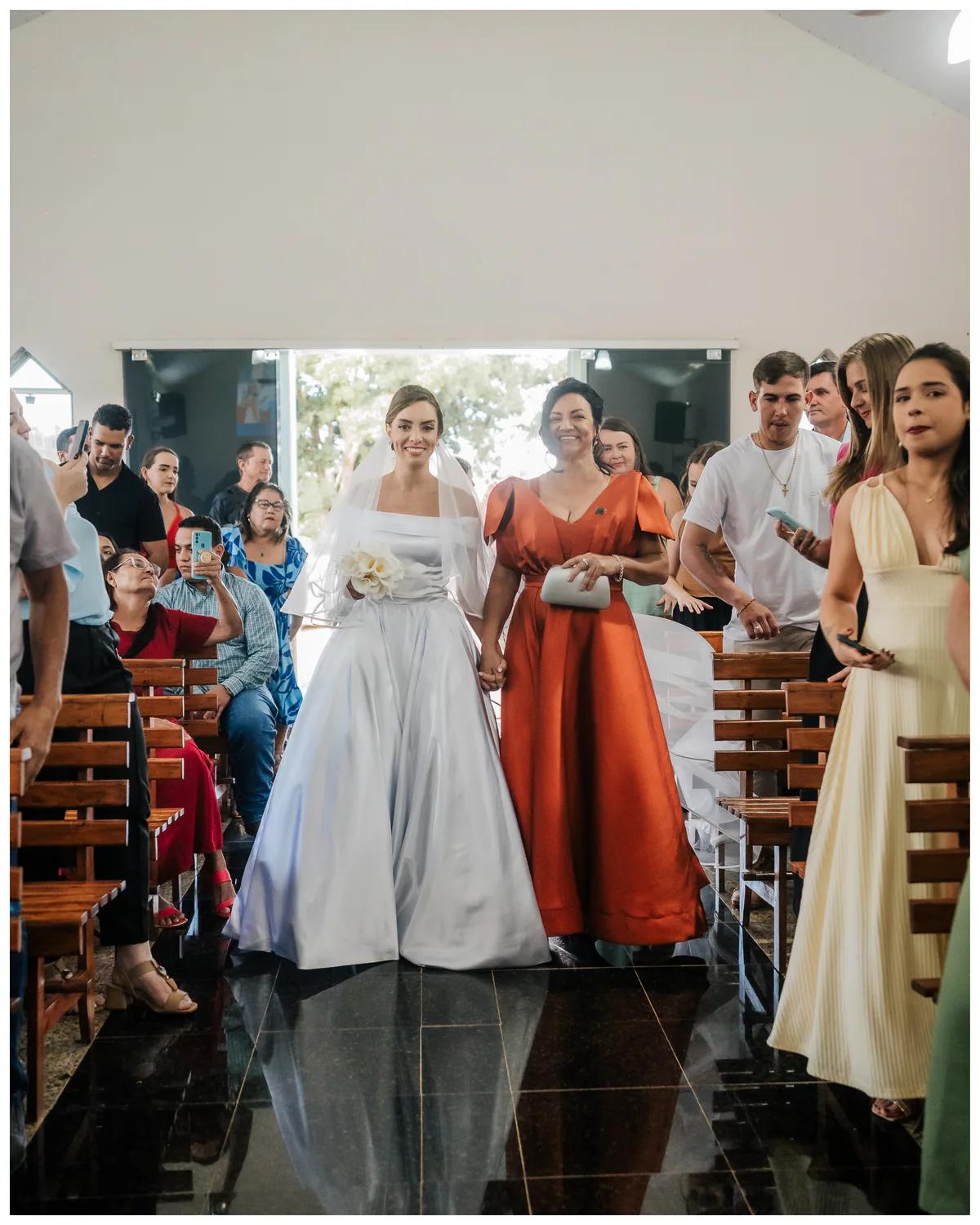 Noiva entra na cerimônia acompanhada por uma mulher de vestido vermelho